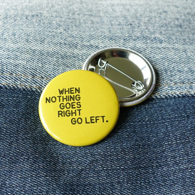 Ansteckbutton When nothing goes right go left auf Jeans mit Rückseite